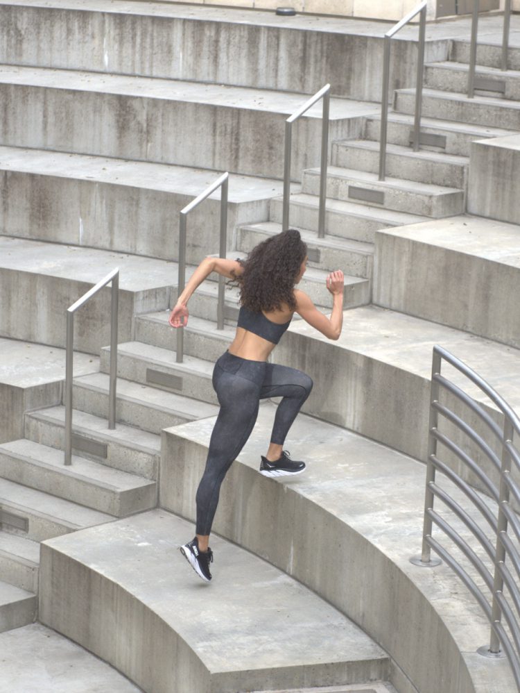 Woman in black athletic wear running up concrete stairs